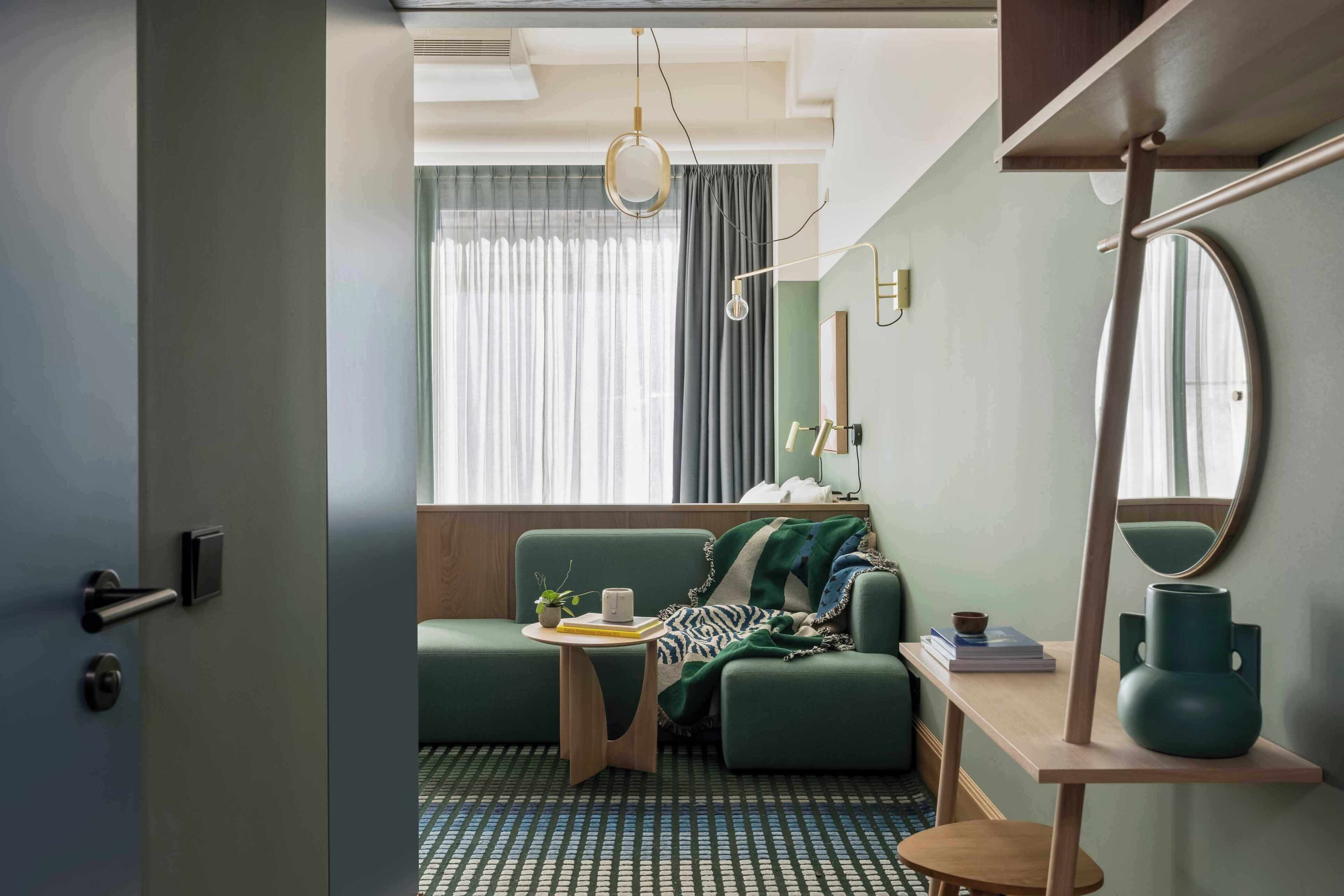 Una habitación con un sofá verde, una mesita de madera, un espejo y un suelo con diseño.