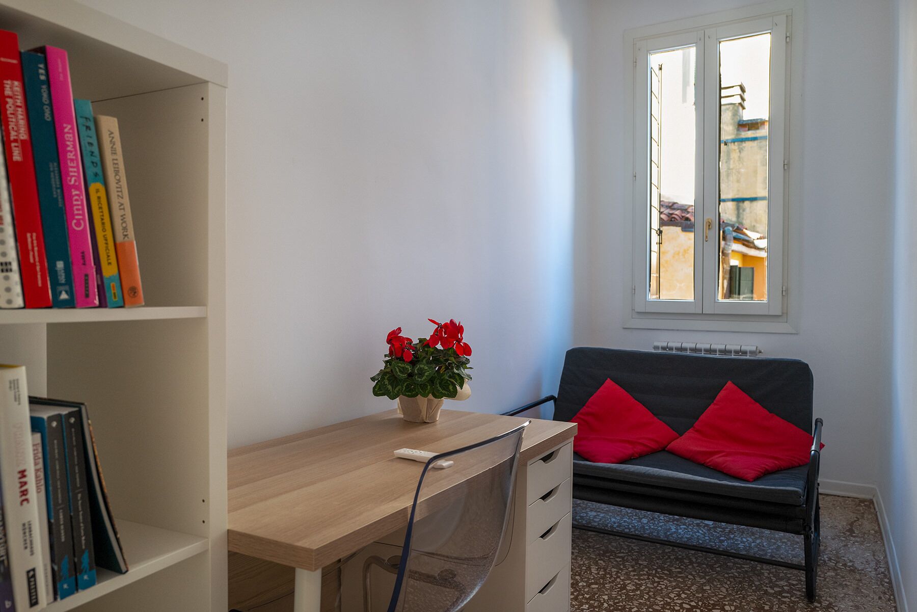 A study room with a desk, bookshelf, and a window with a view of buildings.