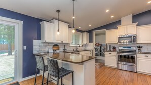 A modern kitchen with white cabinets, stainless steel appliances, and a central island with bar stools. - JACI97-Dog-Friendly Retreat Near Sunriver | Firepit + Fenced Yard (Sunriver)