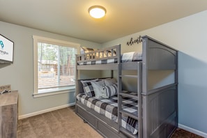 A bunk bed room with a window, a framed sign on the wall, and a small wooden dresser.