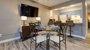 Un espace repas moderne avec une table en verre, quatre chaises, un ventilateur de plafond et un téléviseur à écran plat fixé au mur.