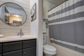 Une salle de bain avec un lavabo blanc, des meubles noirs, un miroir rond, un rideau de douche à rayures et des toilettes blanches.