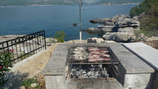 Ein Grill mit Fisch und Fleisch, mit Blick auf einen See, im Hintergrund Berge.