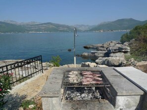 Ein Grill mit Fisch und Fleisch, mit Blick auf einen See, im Hintergrund Berge.