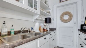 A kitchen with white cabinets, a granite countertop, a double sink, and a door with a wreath. - Southern Belle on Oglethorpe Square (Savannah)