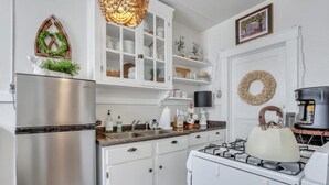 A kitchen with white cabinets, a stainless steel refrigerator, a gas stove, and a hanging light fixture. - Southern Belle on Oglethorpe Square (Savannah)