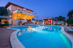 A swimming pool with lounge chairs and a bar area, surrounded by a building with a balcony and outdoor seating. - Oliveres - Six Bedroom Villa, Sleeps 12 (Pollença)