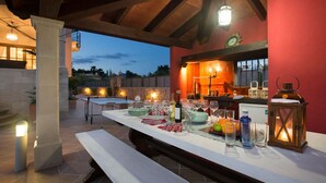 An outdoor dining area with a long table set for a meal, a stone wall, and a view of the landscape. - Oliveres - Six Bedroom Villa, Sleeps 12 (Pollença)