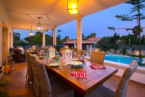 An outdoor dining area with wicker chairs, a wooden table set for dining, and a pool in the background. - Oliveres - Six Bedroom Villa, Sleeps 12 (Pollença)