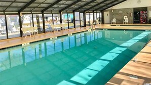 Indendørs swimmingpool med glasvægge, træterrasse og hvide liggestole.