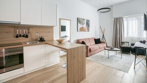 A modern kitchen with white cabinets, a wooden countertop, and stainless steel appliances. There is a dining area with a table and chairs, and a living space with a sofa and a coffee table.