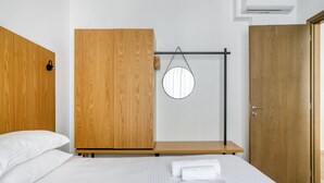 A hotel room with a bed, wooden wardrobe, a round mirror, and a small wooden bench.