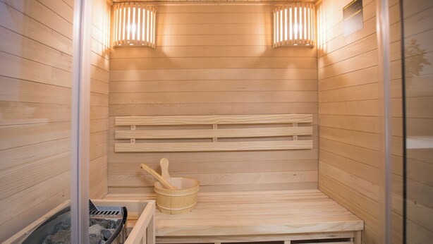 Una sauna con panche in legno, un catino di legno e un recipiente pieno di pietre.