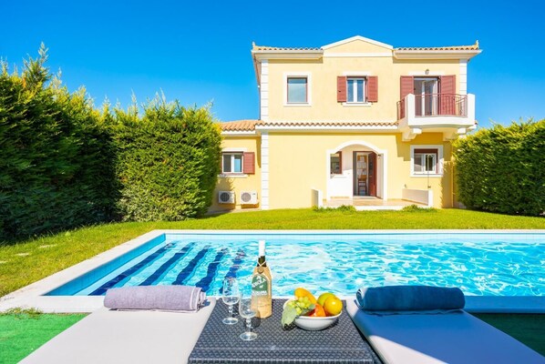 A two-story house with a swimming pool, a patio with a table set for a meal, and a well-maintained lawn.
