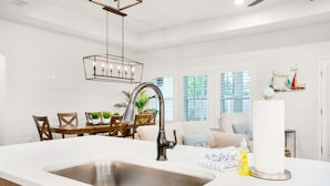 A modern kitchen with a stainless steel sink, wooden dining table, and chairs. There is a chandelier above the sink and a window with a view of greenery outside. - ☀️Private Pool-Walk 2 Beach-Pearl Flamingo☀️ (Panama City Beach)