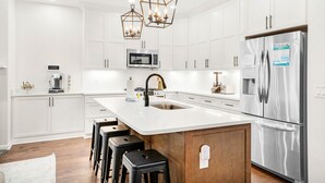 A modern kitchen with white cabinetry, a stainless steel refrigerator, a built-in microwave, and a central island with bar stools. - ☀️Private Pool-Walk 2 Beach-Pearl Flamingo☀️ (Panama City Beach)