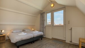 Un dormitorio con dos camas, un radiador, una ventana con cortinas y vistas a edificios.