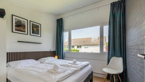 Ein Hotelzimmer mit einem Bett, zwei gerahmten Bildern an der Wand, einem Fenster mit Vorhängen und einem Sessel.