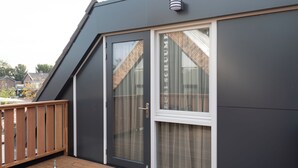 En modern byggnad med en mörk fasad, ett trädäck och en stor skjutdörr i glas med en gardin.