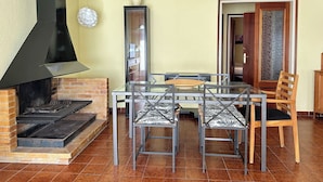 A dining area with a brick fireplace, a glass table, and metal chairs.