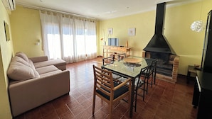 A living room with a sofa, a glass dining table, chairs, a TV, and a fireplace.