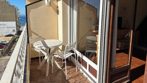 A balcony with a table and chairs, a sliding glass door, and a view of the sea.