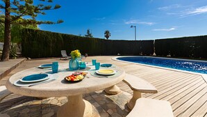 Un área de comedor junto a la piscina, con una mesa para dos, una piscina y un seto al fondo.