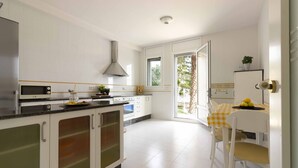 Una cocina moderna con armarios blancos, una campana extractora de acero inoxidable y un comedor con mantel a cuadros amarillos.