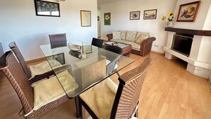 A modern living room with a glass dining table, wicker chairs, a sofa, and a fireplace. - El Moll de Roses - Three Bedroom Apartment, Sleeps 6 (Roses)