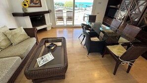 A living room with a glass coffee table, wicker furniture, a fireplace, and a view of the sea. - El Moll de Roses - Three Bedroom Apartment, Sleeps 6 (Roses)