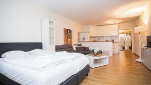 Una habitación de hotel moderna con una cama grande, un sofá pequeño, una mesita de centro y una kitchenette al fondo.