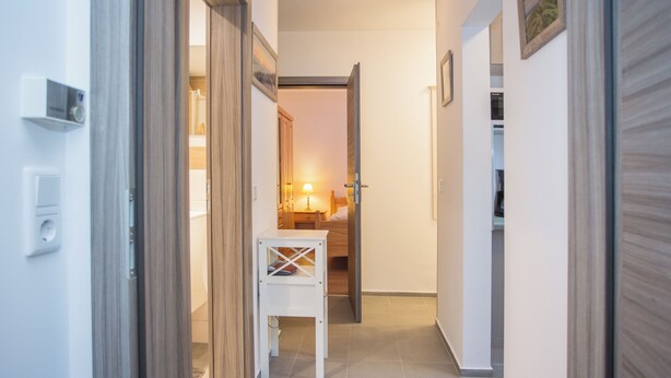 A hallway with a wooden door, a white table, and a bed in the background. - Apt - Am Bergelchen 66-B | Winterberg-Ni (Winterberg)