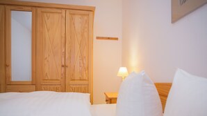 A hotel room with a wooden wardrobe, a bedside table with a lamp, and a bed with white bedding. - Apt - Am Bergelchen 66-B | Winterberg-Ni (Winterberg)