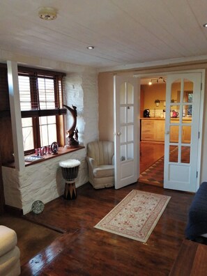 Cozy room with a wooden floor, white walls, and a large window offering a view of the adjacent kitchen.