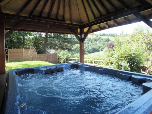 Relax in a serene hot tub under a shaded pergola surrounded by lush greenery.