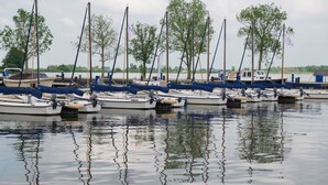 Un port de plaisance où plusieurs voiliers sont amarrés dans une eau calme, entourés d’arbres et sous un ciel dégagé.