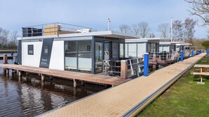 Une maison flottante moderne dotée d’un quai, de grandes fenêtres et d’une plaque signalétique portant l’inscription « Marin Home ».