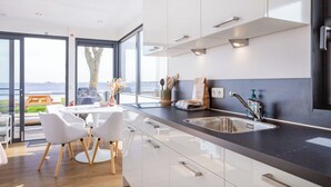 Une cuisine moderne dotée d’une grande fenêtre, de meubles blancs et d’un évier en acier inoxydable.