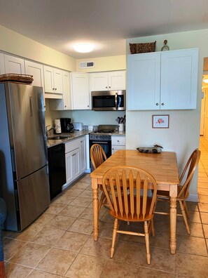 A kitchen with white cabinets, a stainless steel refrigerator, a microwave, a stove, and a wooden dining table with chairs.