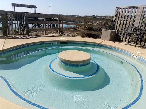A swimming pool with a circular hot tub in the center, surrounded by a wooden deck and a wooden fence.