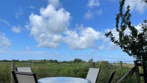A round table with four chairs, a wooden fence, and a grassy field under a blue sky with clouds. - Cosy, self-contained rural bungalow – peaceful countryside escape (Out Rawcliffe Preston)