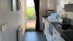 A narrow kitchen with white cabinets, a black countertop, and a view through a door to a garden. - Cosy, self-contained rural bungalow – peaceful countryside escape (Out Rawcliffe Preston)