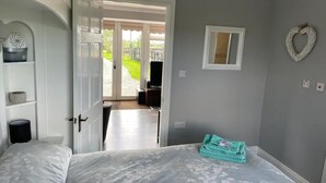 A bedroom with a bed, a door leading to a balcony, a small mirror, and a heart-shaped decoration on the wall. - Cosy, self-contained rural bungalow – peaceful countryside escape (Out Rawcliffe Preston)