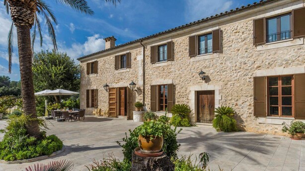 A stone building with multiple windows and doors, a courtyard with outdoor seating, and a palm tree. - Cadell Gran - Seven Bedroom Villa, Sleeps 14 (La Puebla)