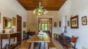 A spacious dining area with a long wooden table, benches, and chairs. There are framed pictures on the walls, a chandelier, and a stone wall. - Cadell Gran - Seven Bedroom Villa, Sleeps 14 (La Puebla)