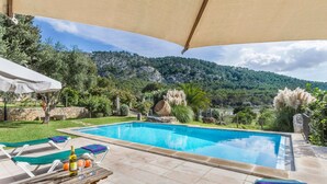 A pool area with lounge chairs and a table, surrounded by greenery and a mountainous backdrop. - Cadell Gran - Seven Bedroom Villa, Sleeps 14 (La Puebla)