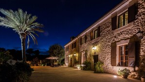 A stone building with multiple windows and a well-lit outdoor patio area. - Cadell Gran - Seven Bedroom Villa, Sleeps 14 (La Puebla)