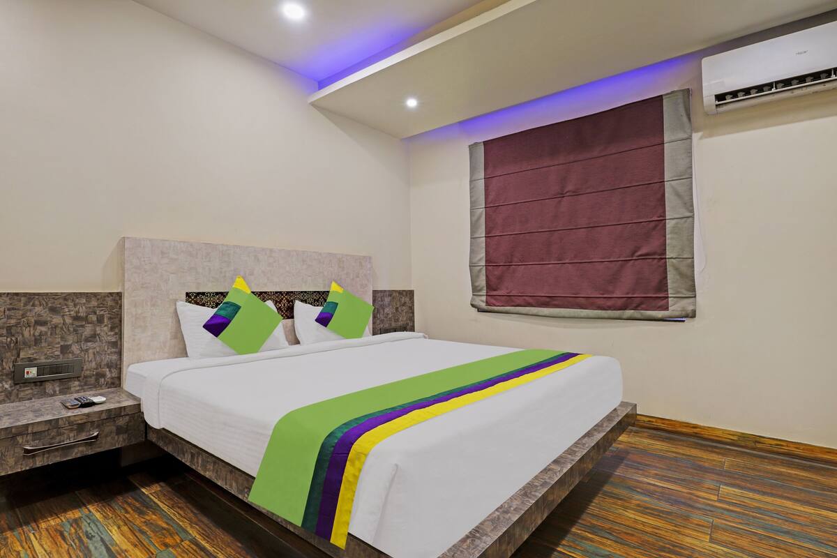 A hotel room with a bed, nightstand, and an air conditioning unit.
