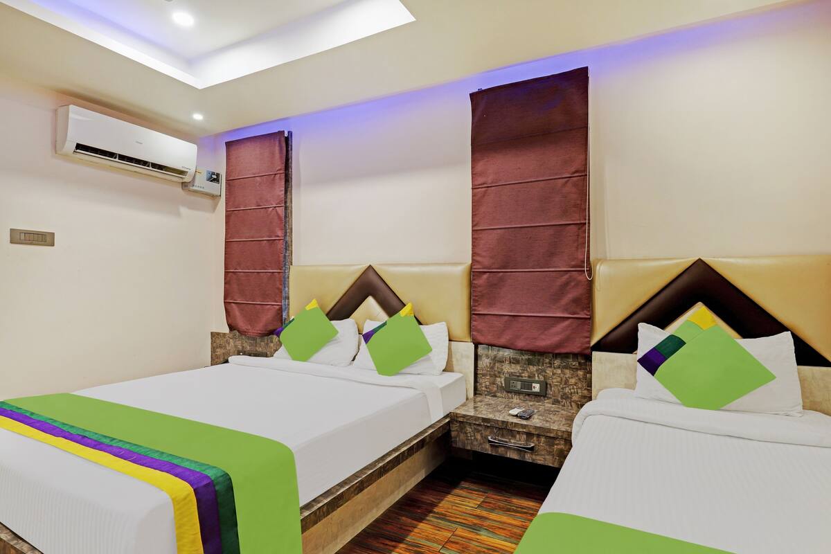 A hotel room with two beds, a small desk, and an air conditioning unit on the wall.