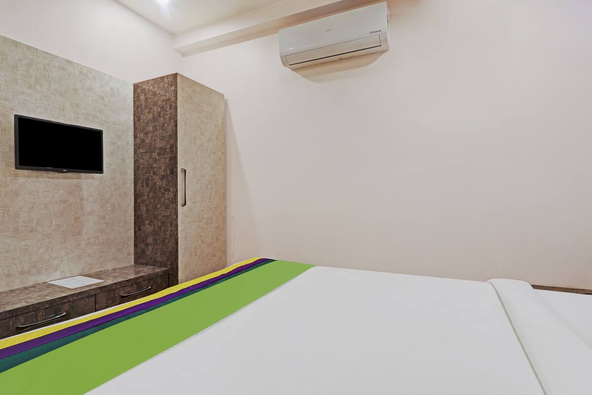 A bedroom with a bed, a TV mounted on the wall, a wardrobe, and an air conditioner.